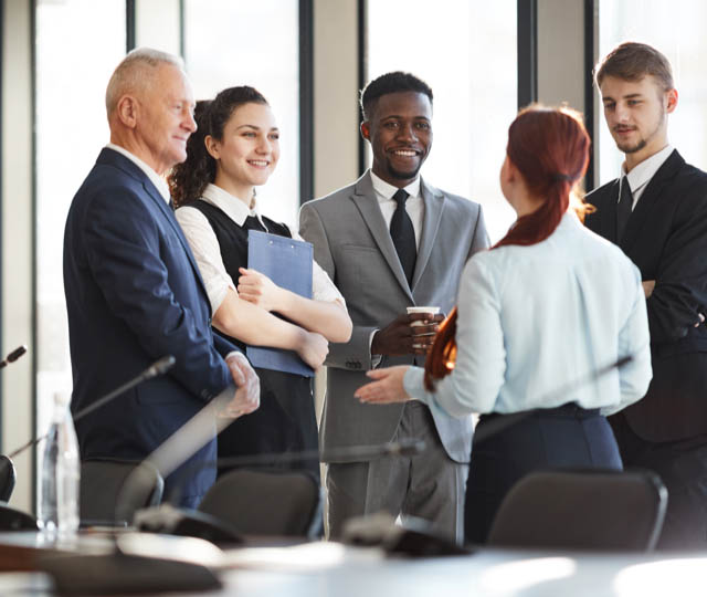 Multi-ethnic group of cheerful business people standing by window in office and communicating.