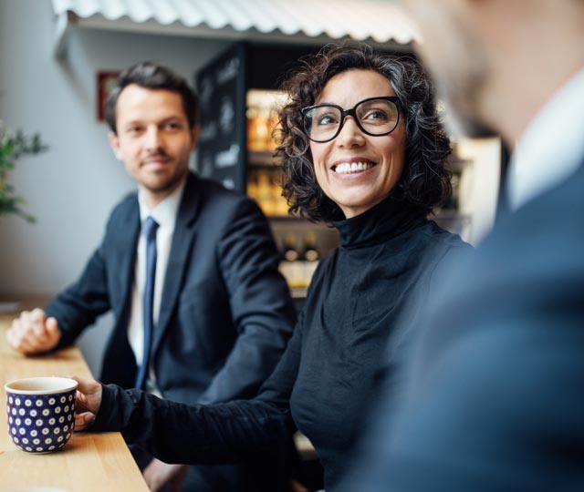 Une femme et un homme souriants, assis à une table, discutent avec un autre homme.