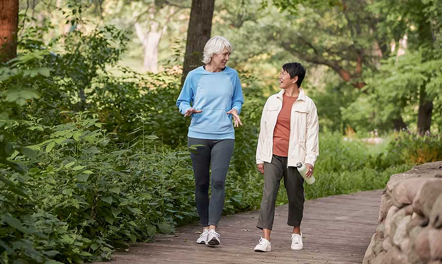 Two women walking in park briskly and talking