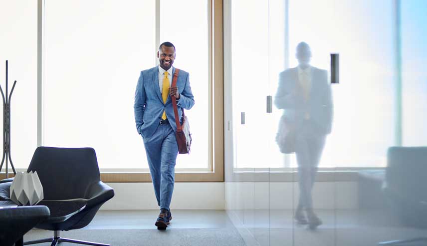 Professional man walking down the hallway smiling with his refection on the wall.